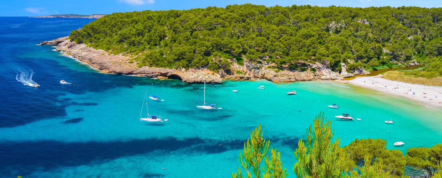 Yachtcharter Menorca - Türkisblaue Bucht mit Segelbooten und grüner Küstenlandschaft