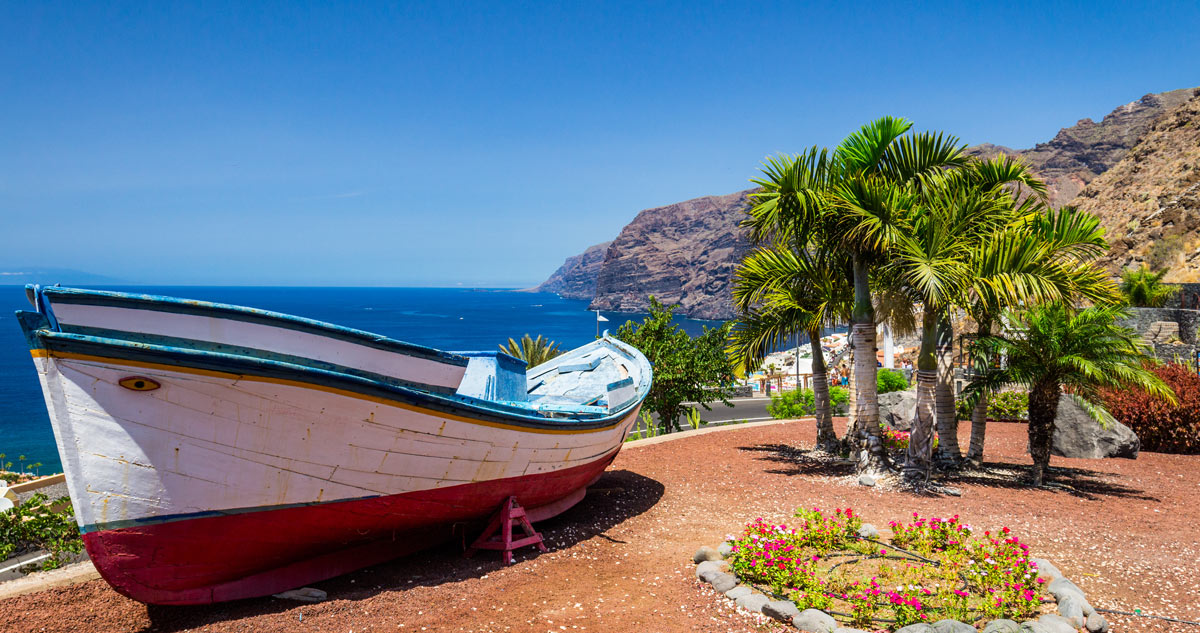 Blick auf die Steilküste Los Gigantes auf Teneriffa – Palmen, Atlantik und ein altes Fischerboot erzählen vom maritimen Leben der Kanaren.